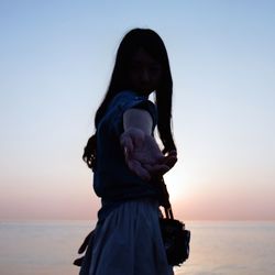 Woman overlooking calm sea with hand stretched out