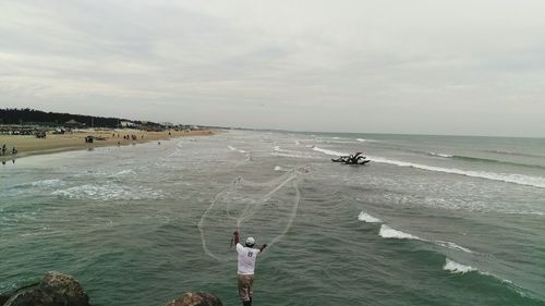 High angle view of fisherman throwing net in sea against sky