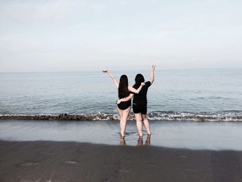 Rear view of friends standing at beach against sky