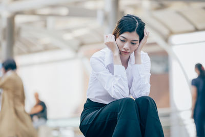 Low angle view of thoughtful young woman sitting outdoors