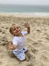 Cute baby boy with messy hands kneeling at beach
