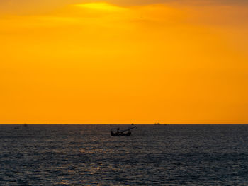 Silhouette person in sea against orange sky