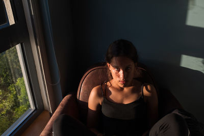 Teenage girl is sitting on the armchair. a warm natural light illuminates a part of her face.