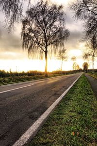 Road by trees against sky during sunset