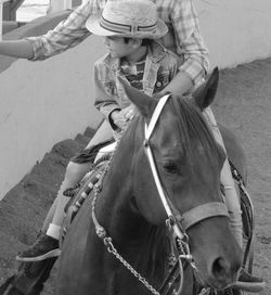 Son in hat with father riding horse