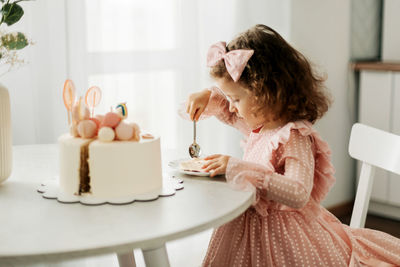 Cute little girl eats a birthday cake with a spoon on her birthday