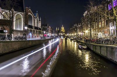 Light trails in canal amidst buildings in city against clear sky
