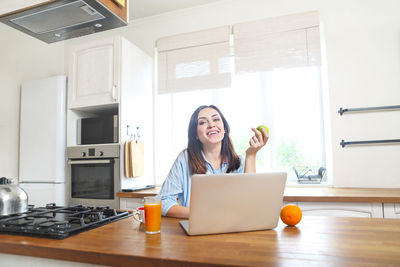 Cheerful woman using laptop in kitchen at home