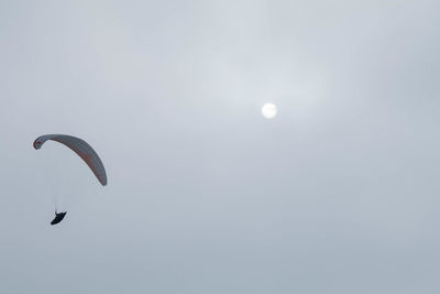 Low angle view of people paragliding against sky