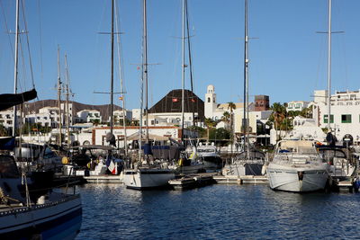 Sailboats moored in harbor by city against clear sky