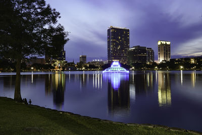 Illuminated buildings by lake against sky in city at night