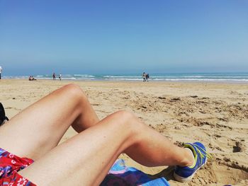 Midsection of woman relaxing on beach against sky