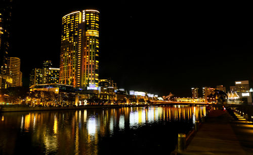 Illuminated buildings by river against sky at night