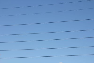 Low angle view of power lines against blue sky