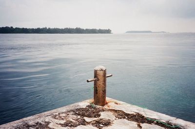 Bollard on pier by sea against sky