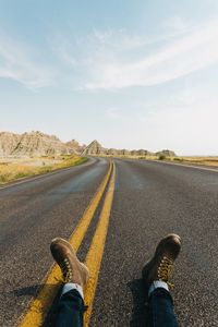 Low section of man sitting on road against sky