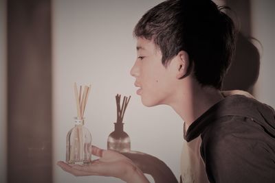 Side view of boy holding container with sticks against wall at home