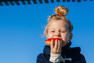 Portrait of woman eating ice cream against blue sky