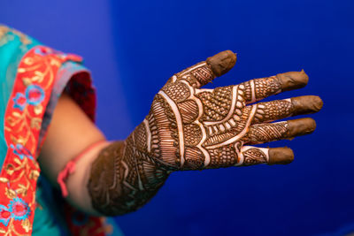 Midsection of bride with henna tattoo against blue background