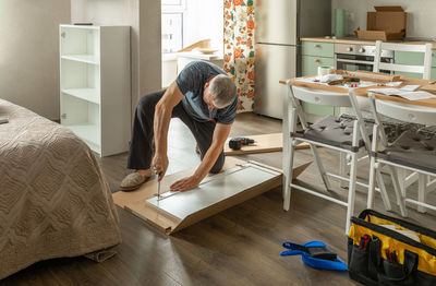 A man at home collects furniture with an electric screwdriver.