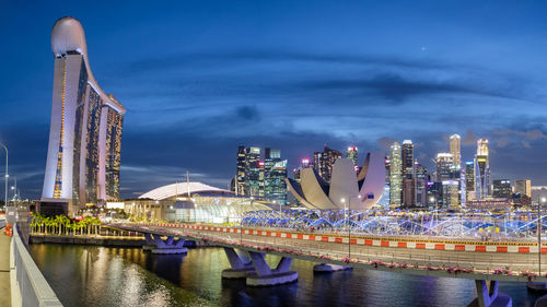 Illuminated modern buildings by river against sky at night