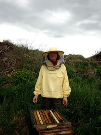 Portrait of female bee keeper standing on field against sky