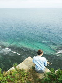 Rear view of man sitting on rock by sea