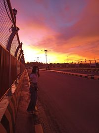 Rear view of man walking on road against sky during sunset