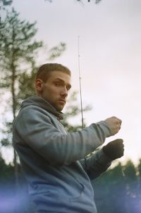 Portrait of man with fishing rod by trees against sky