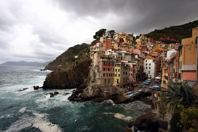 Buildings by sea against cloudy sky