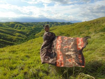 Woman wrapped in shawl standing on field against sky