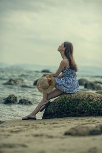 Side view of young woman standing against sky