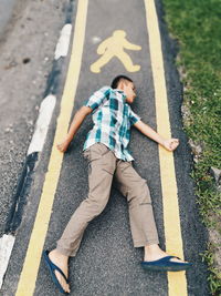 High angle view of boy imitating pedestrian sign on road