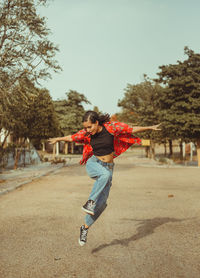 Full length portrait of boy jumping on tree against sky