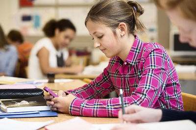 Schoolgirl using mobile phone at desk in classroom