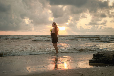 Silhouette woman standing at beach against sky during sunset