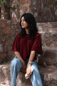 Portrait of young woman sitting on retaining wall