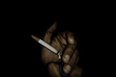 Midsection of man holding cigarette against black background