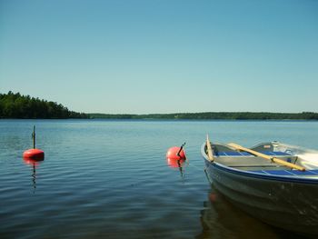 Boats moored in lake against clear blue sky