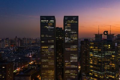 Illuminated buildings in city against sky at dusk