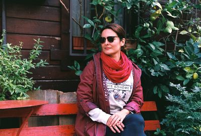 Smiling woman sitting on bench amidst plants at yard