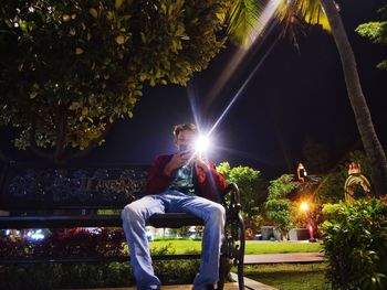 Man sitting by illuminated tree at night