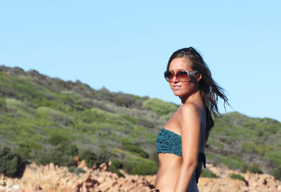 Portrait of smiling young woman standing on landscape against clear sky