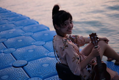 Portrait of woman with guitar sitting at beach