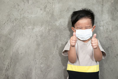 Portrait of boy standing against wall covered with face