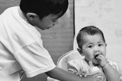 Boy giving milk bottle to sister sitting at home