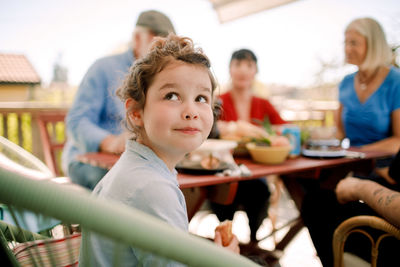 Smiling girl looking up while sitting with family at table in patio