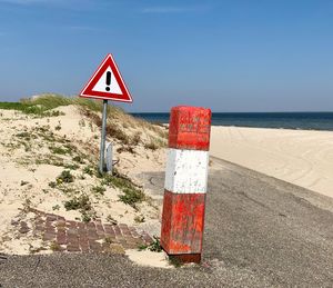 Road sign by sea against clear sky