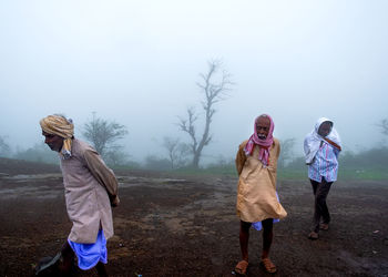 Rear view of people on field against sky during winter