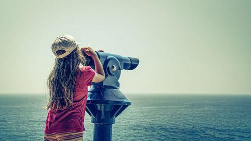 Rear view of girl looking sea through coin-operated binoculars